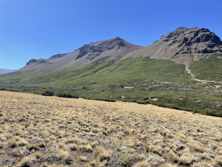 Dry golden grass below a green slope and two rocky summits