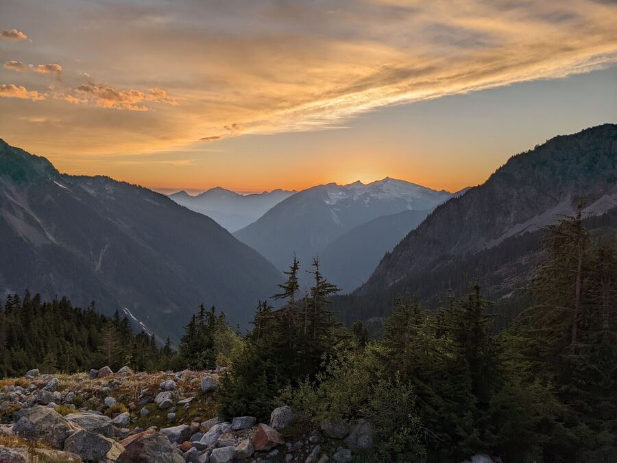 An orange sunset over layered mountain ridges and a rocky slope