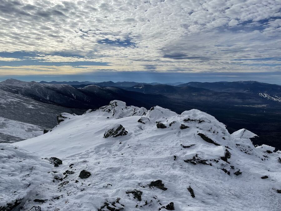 Snow-covered rocks on a summit under a textured grey sky
