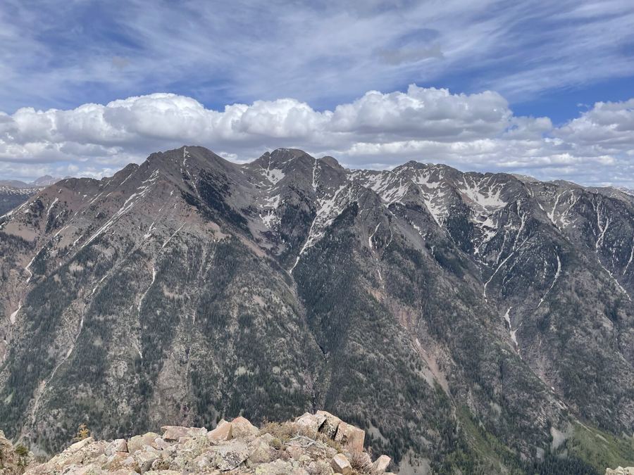 A steep mountain face streaked with snow under a long band of cloud